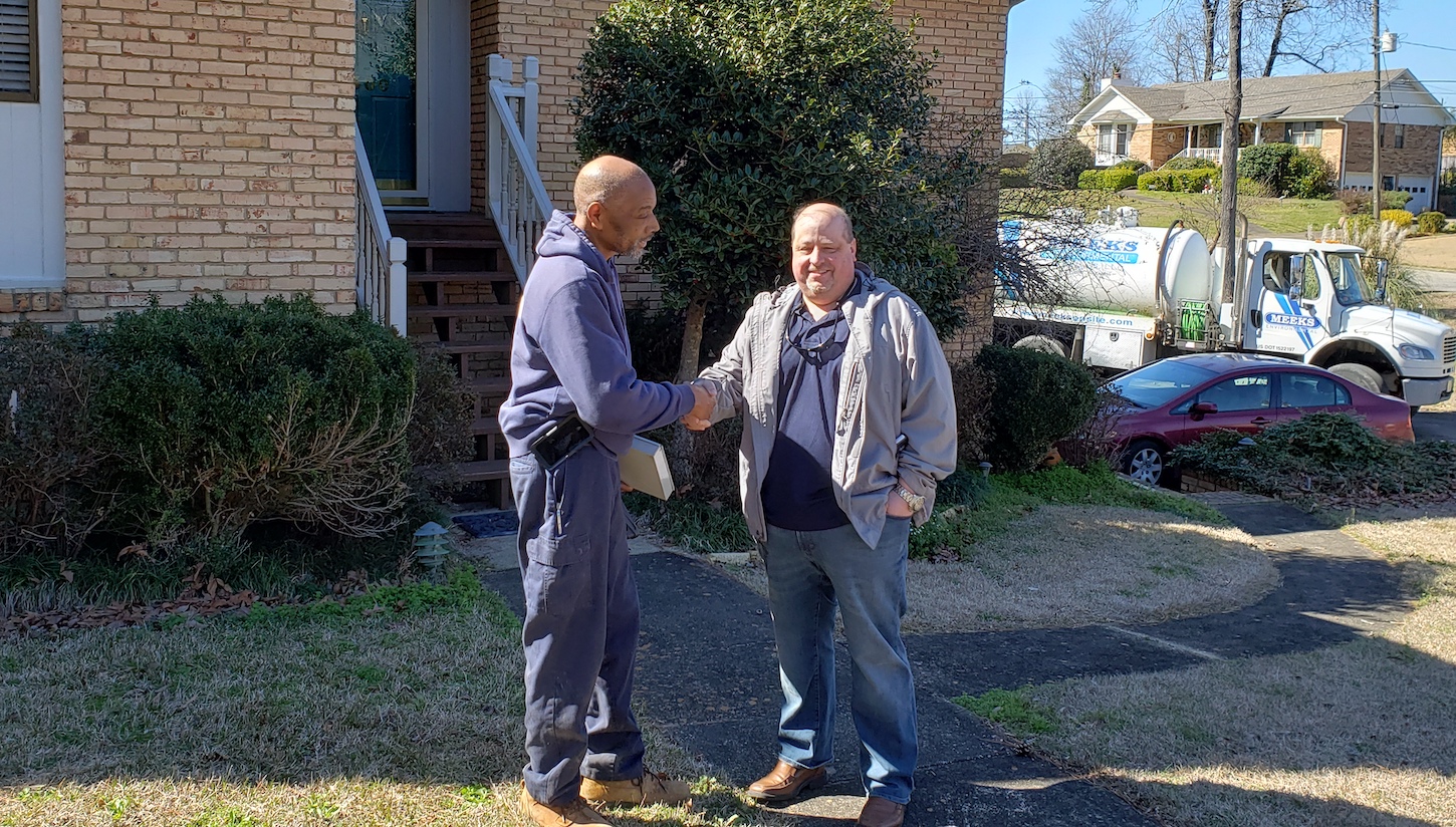 Meeks technician shaking hands with a homeowner in front of a brick house