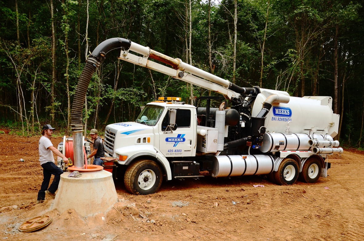 Meeks vacuum truck with boom hose working at a manhole in a cleared wooded site
