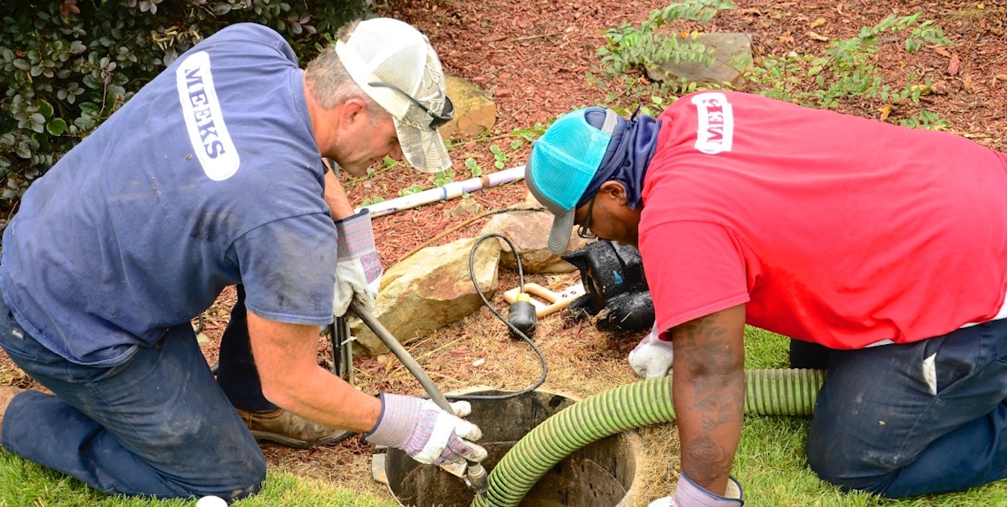 Two Meeks crew members servicing a septic tank access in a lawn