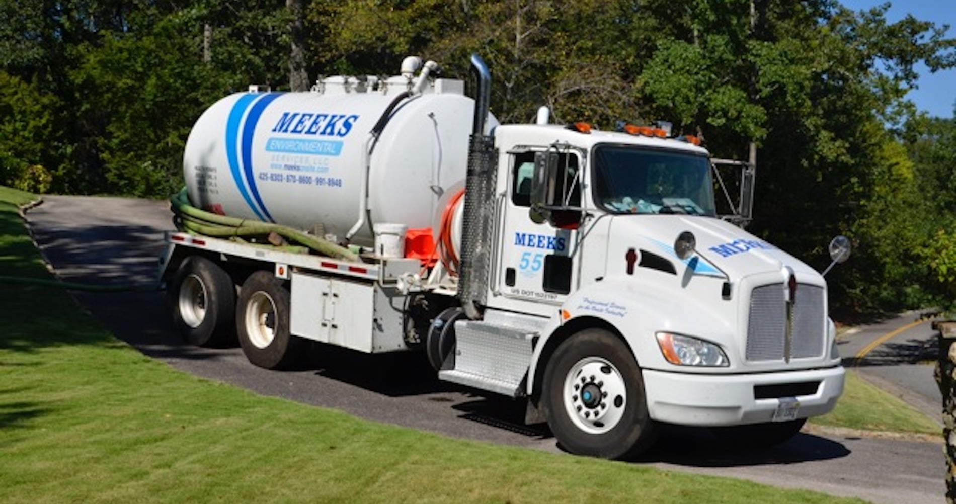 Meeks septic truck with hose and tank leaving a residential driveway